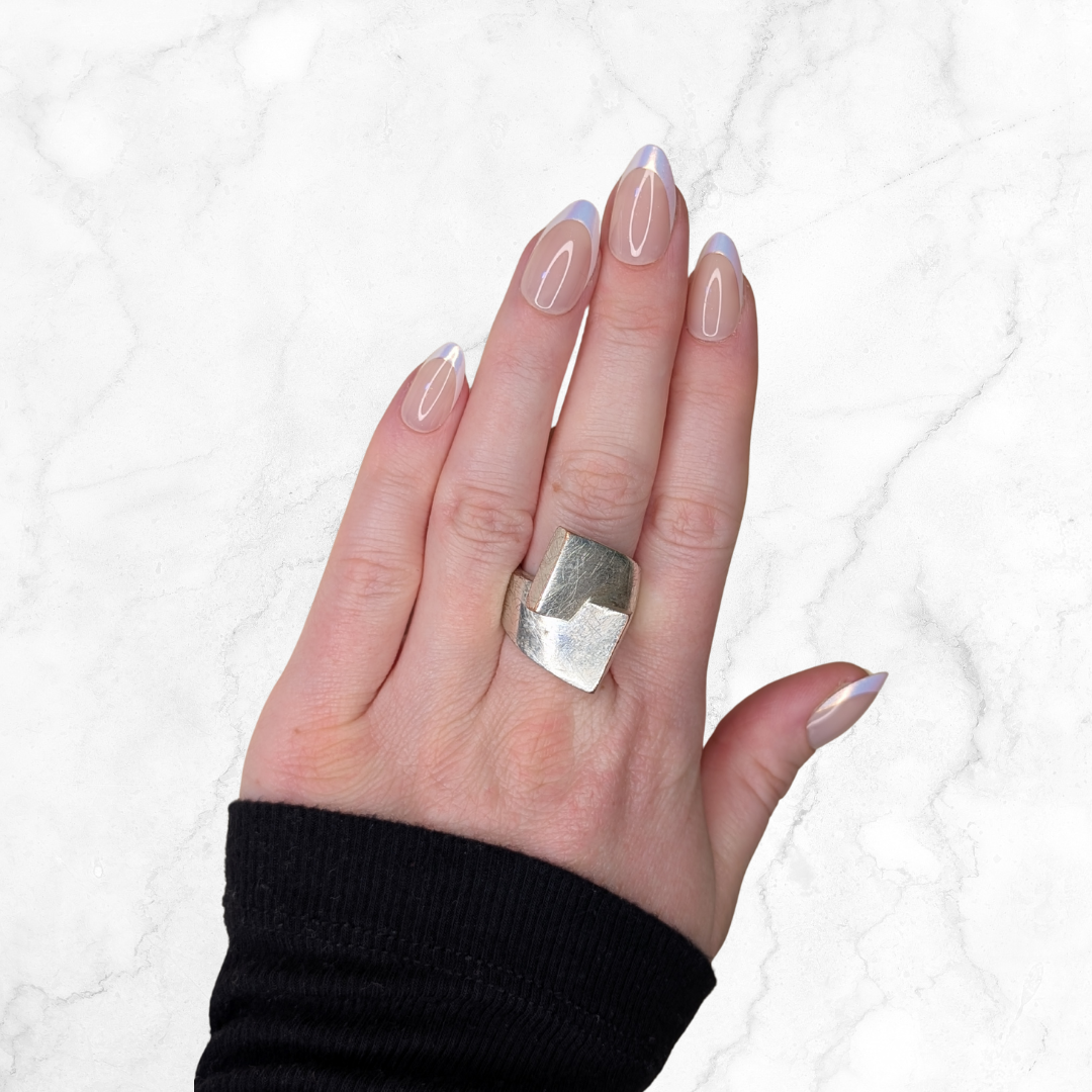 Left hand showing shimmery almond french tipped nails on a marble background.