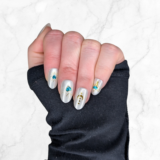 Image of a left hand wearing Snap Nails in Signature collection of 5 oval pearl nails gold details on a marble background.
