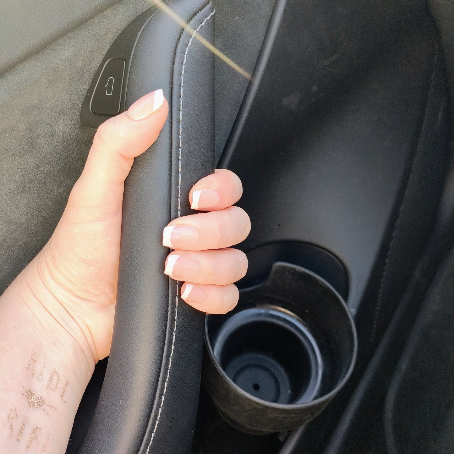 Left hand showing classic square French tipped nails holding onto a car handle.