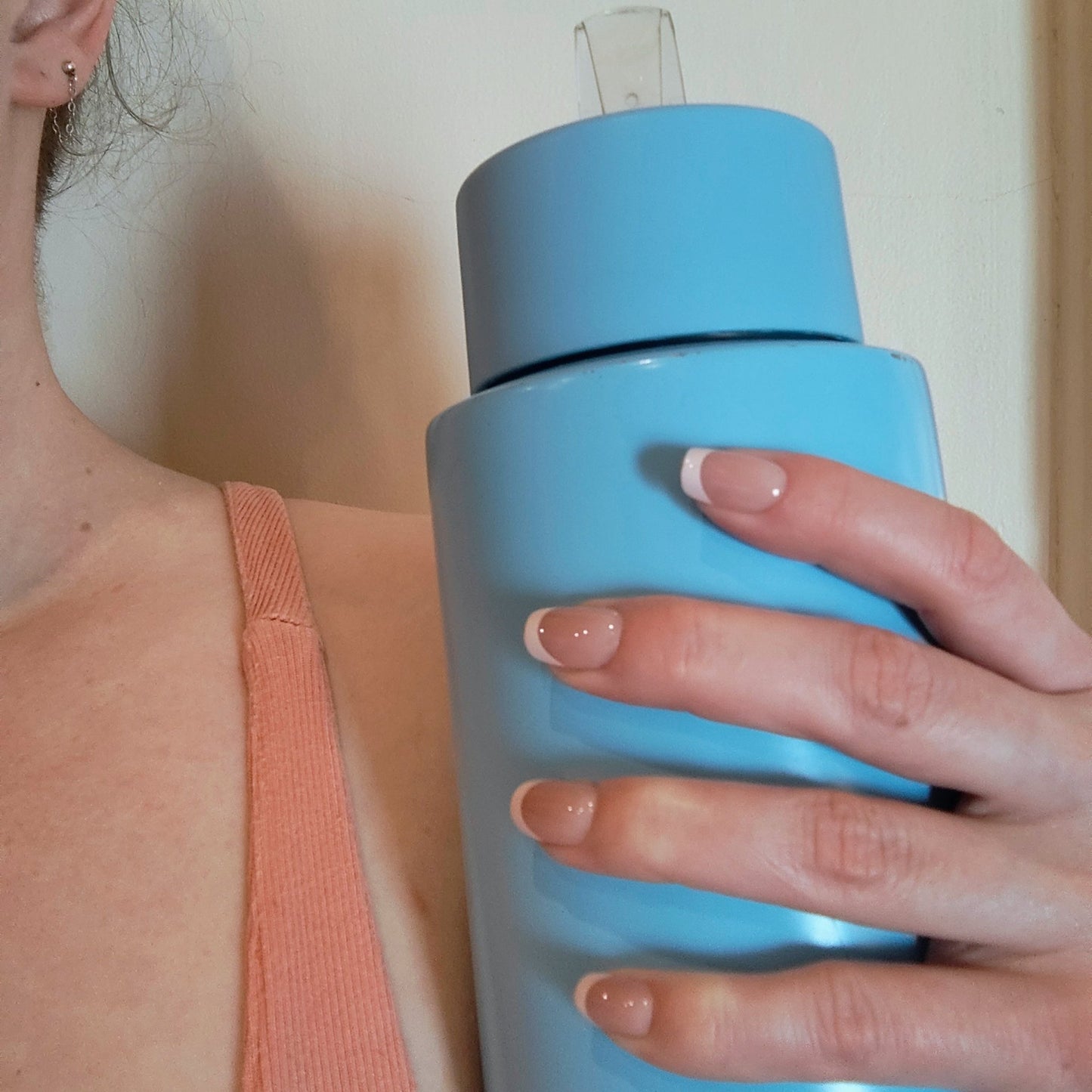 Left hand showing classic square French tipped nails holding a blue water bottle.