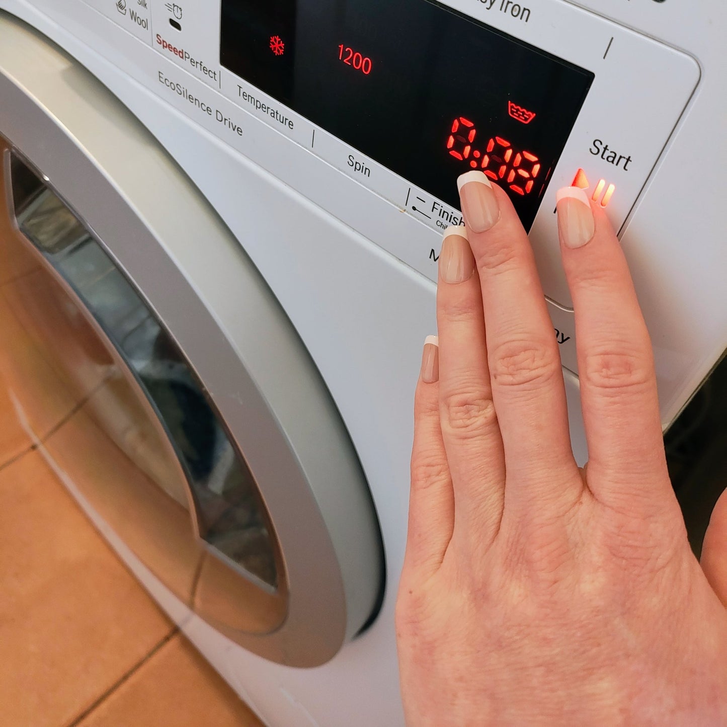 Left hand showing classic square French tipped nails pressing a washing machine button.