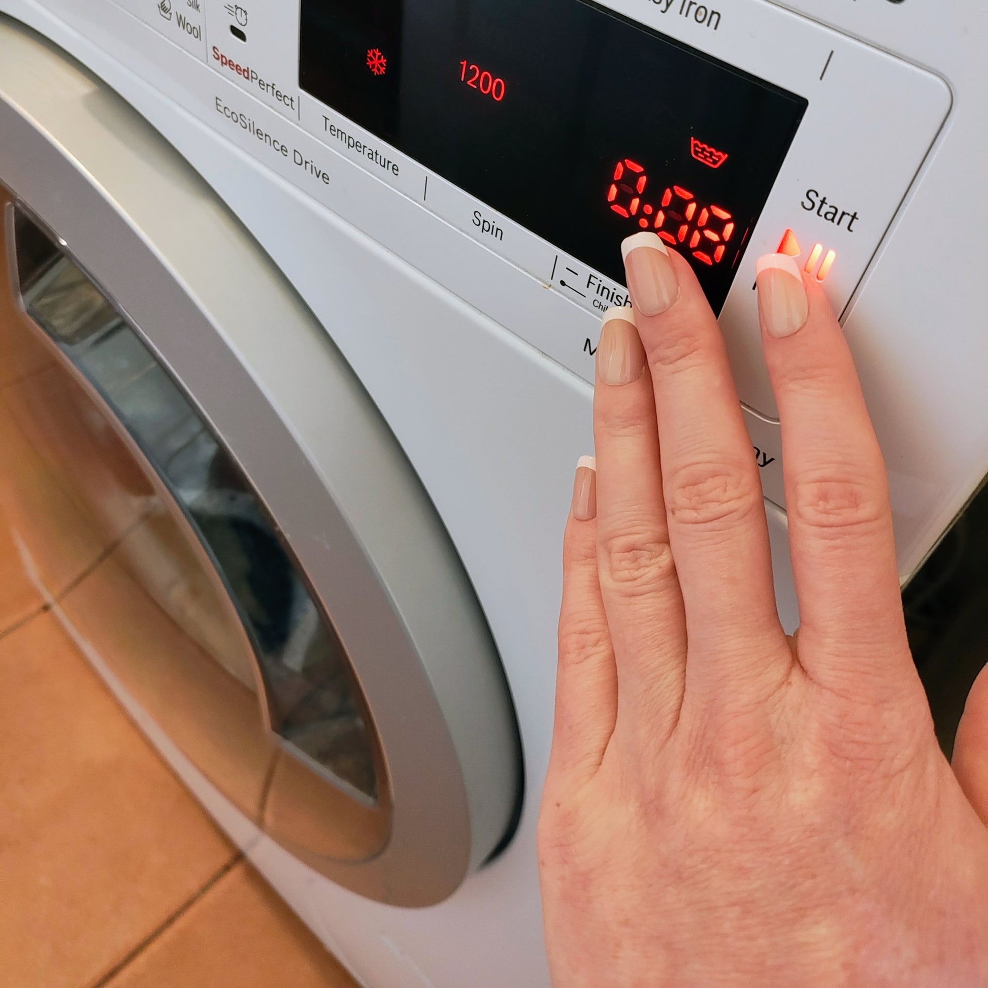 Left hand showing classic square French tipped nails pressing a washing machine button.