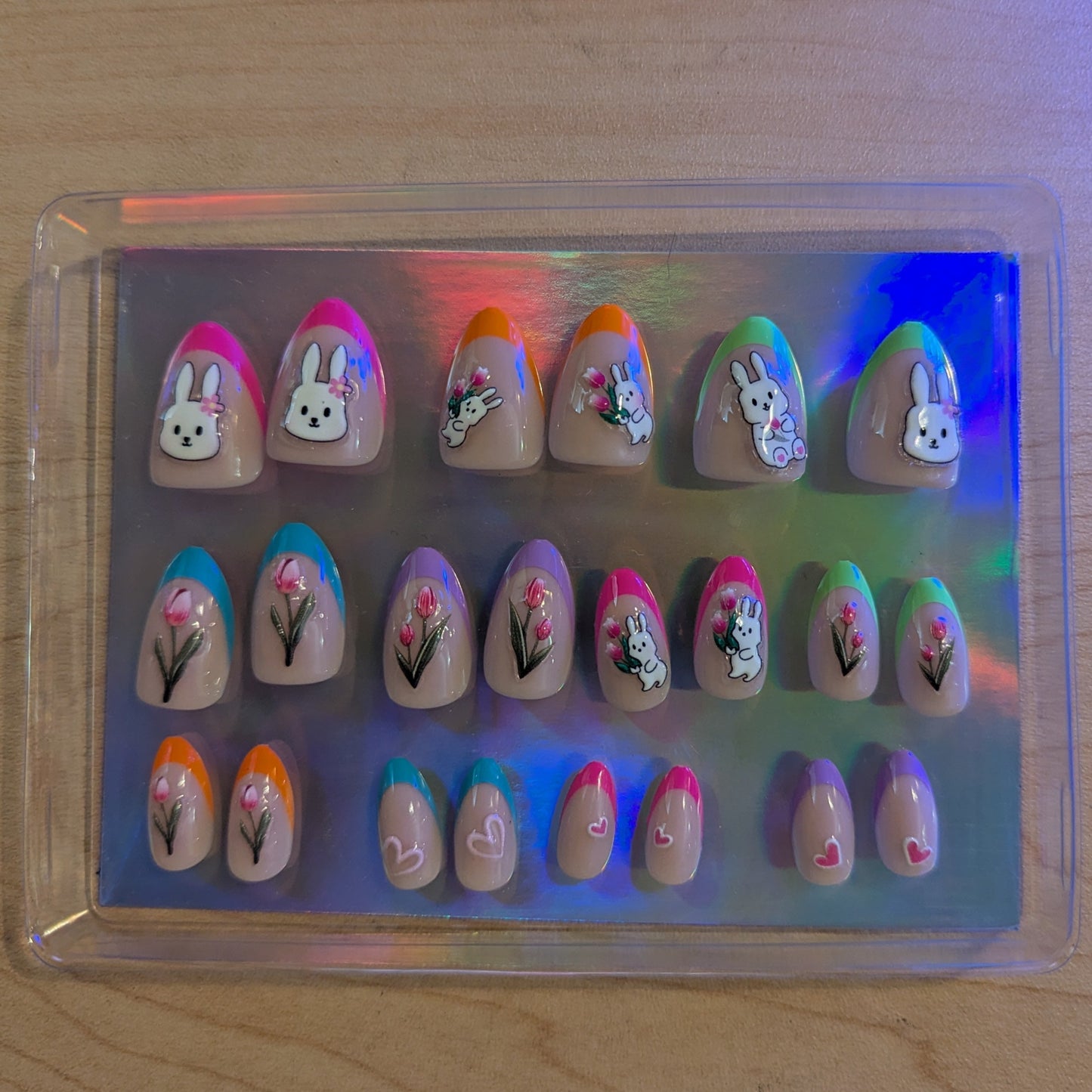 A clear box with almond gel press-ons with 22 nails of varying tip colours and Easter designs.