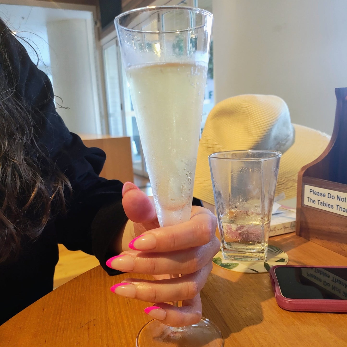 Left hand showing almond nails with a hot pink French tip holding a sparkling wine glass at a pub.