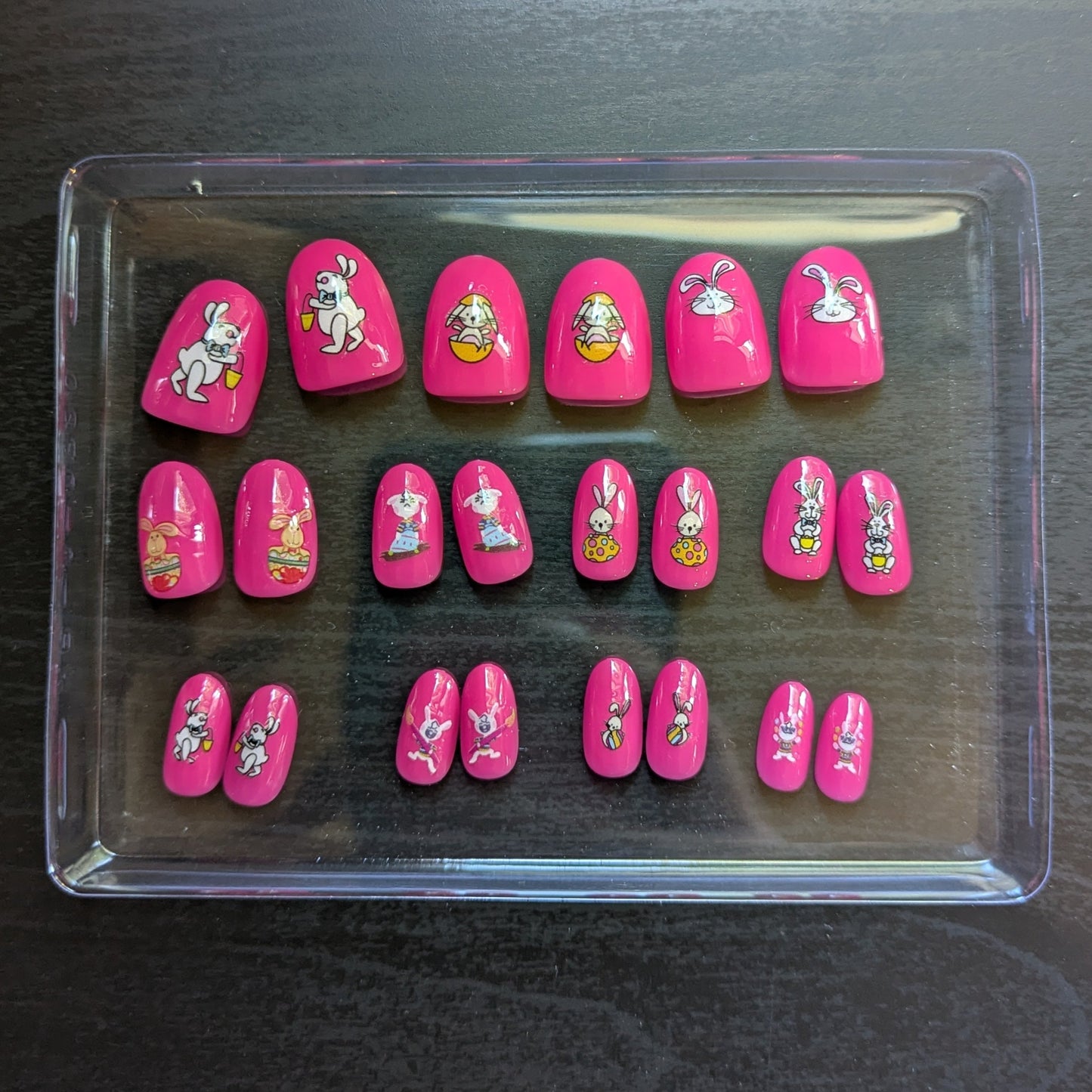 Image of a clear box with 22 oval hot pink press on gel nails with various Easter designs.