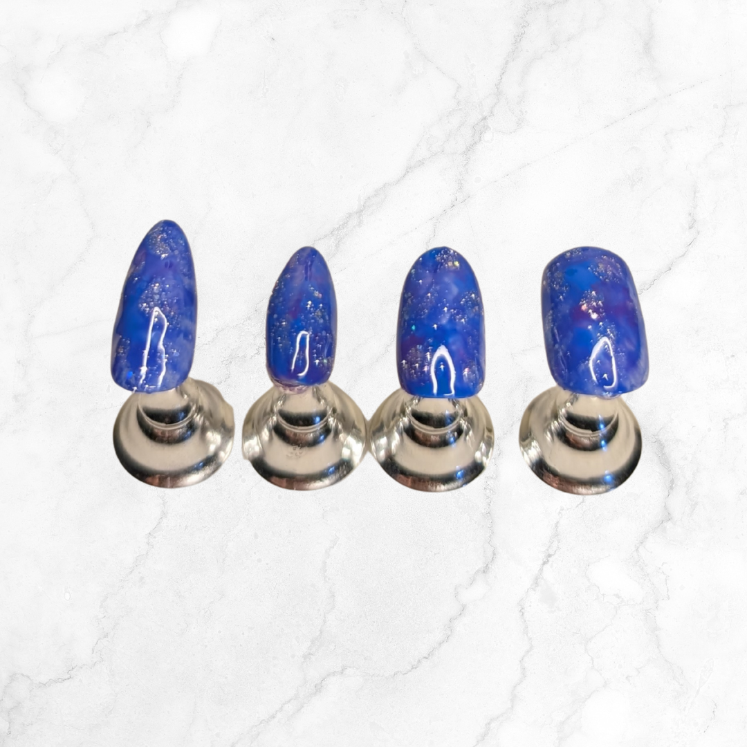 Four nails wearing blue and purple marbled press-on nails with silver sparkle in a long and short almond shape., square and oval shapes.