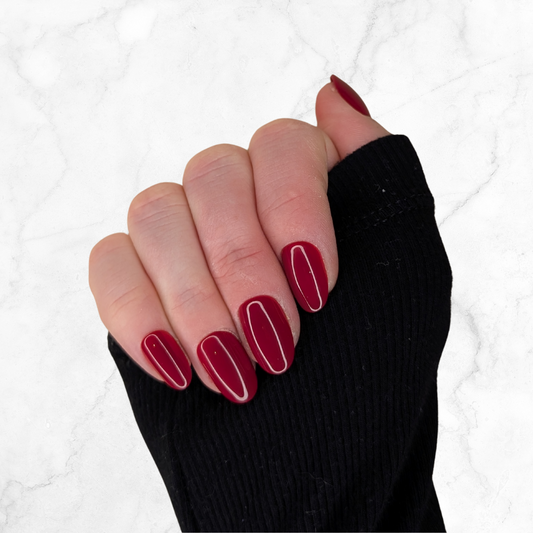 Right hand wearing oval deep red nails on a marble background.