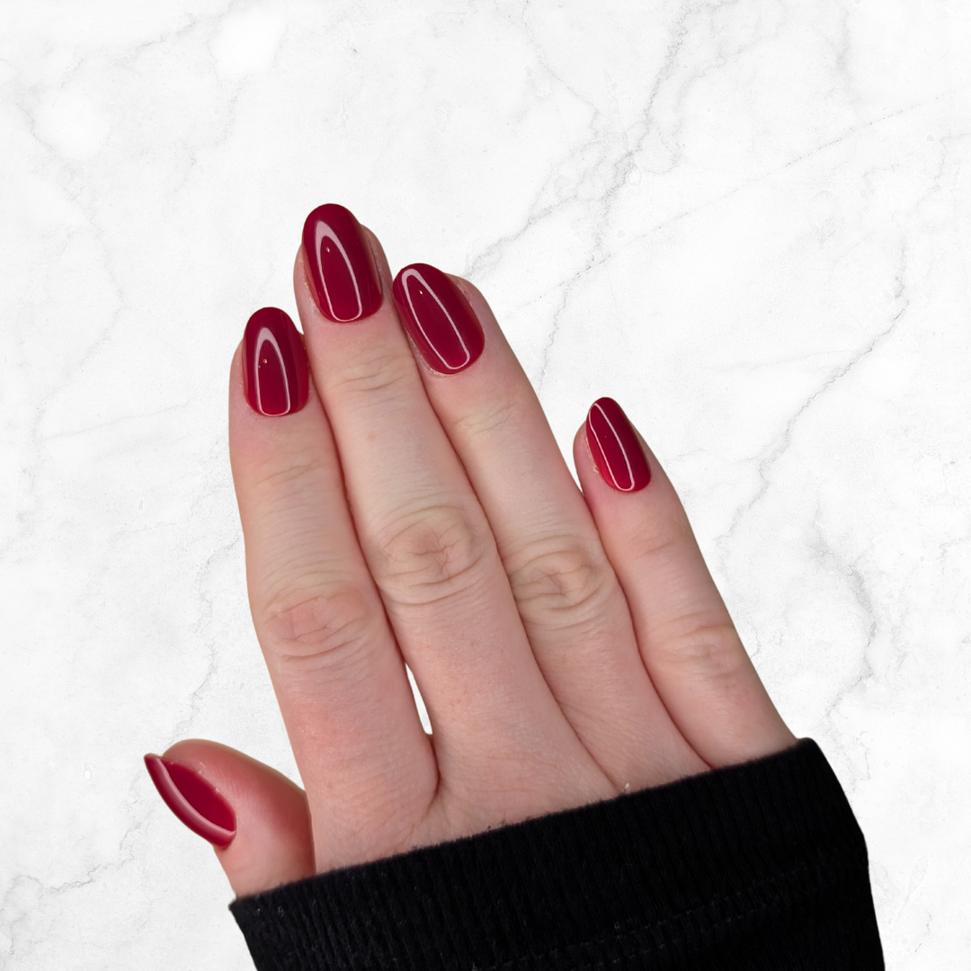 Right hand wearing oval deep red nails on a marble background.