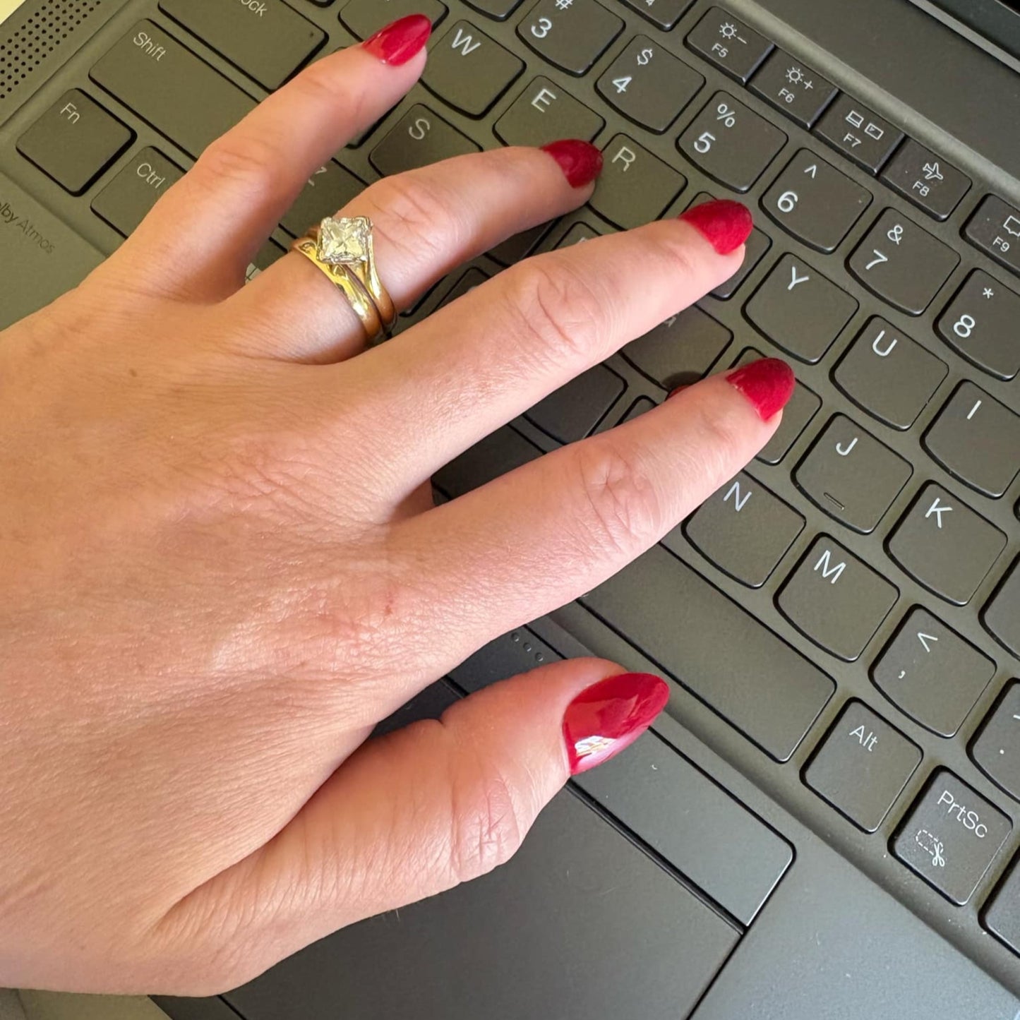 Left hand showing deep red oval shaped nails on a laptop keyboard.