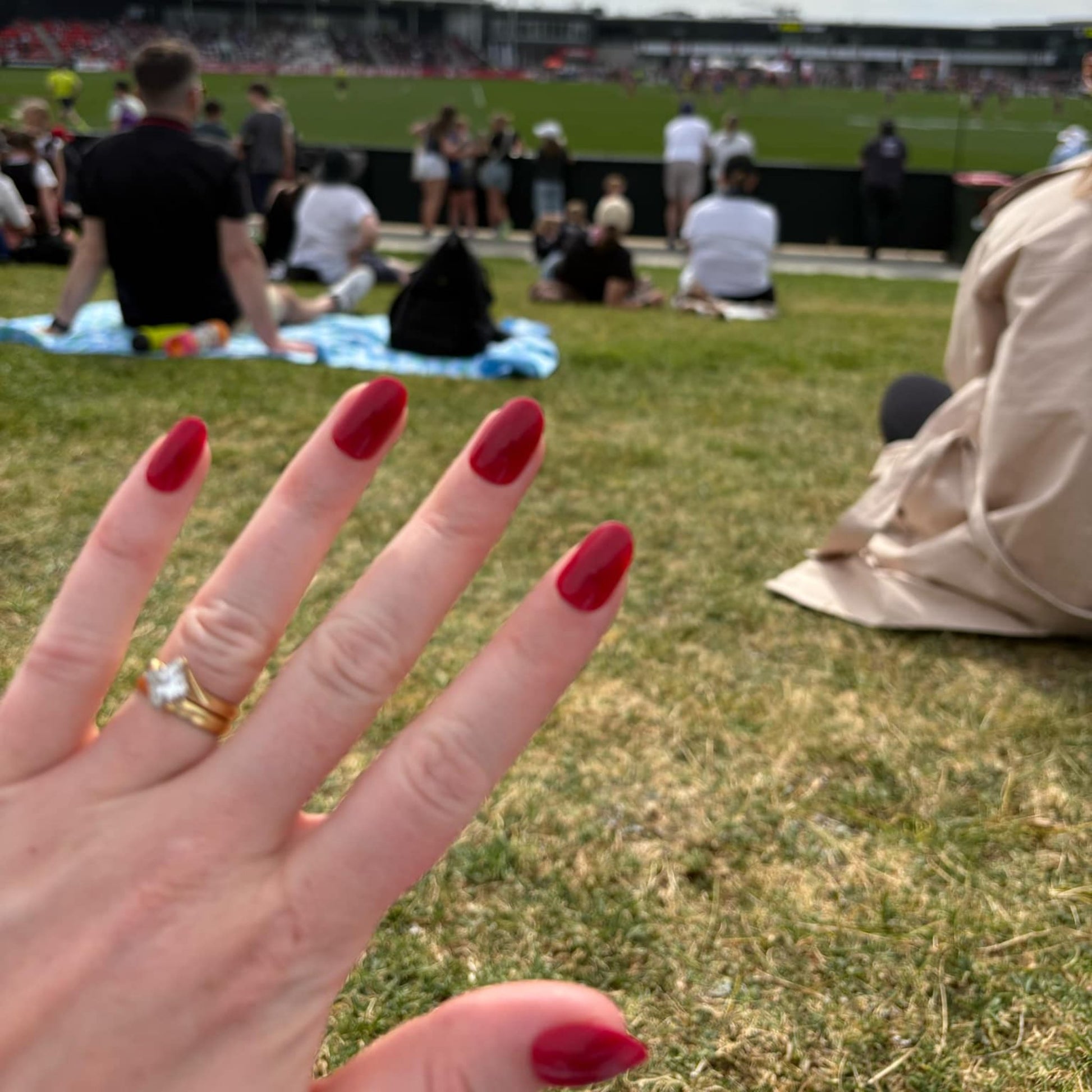 Left hand showing deep red oval shaped nails on a hill looking at a football game.