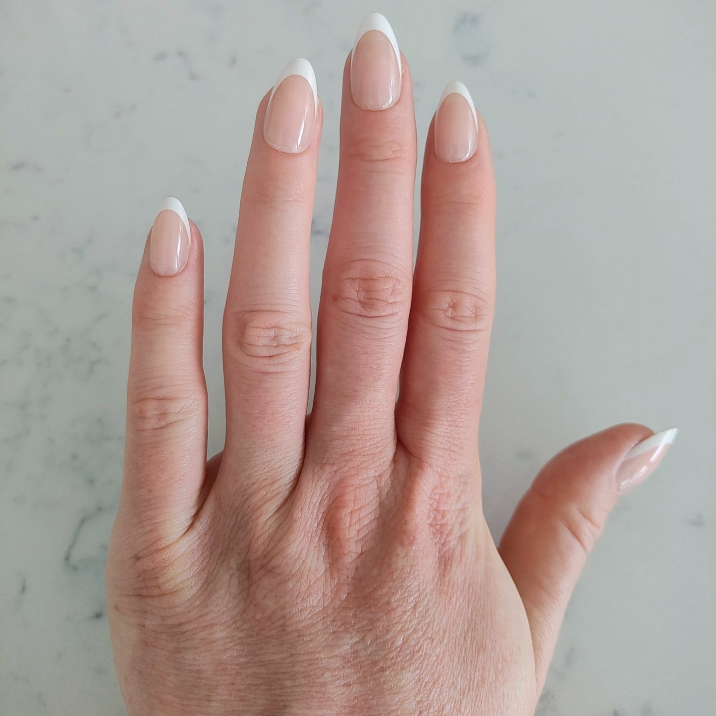 Left nail showing a classic almond French tip on a marble background.