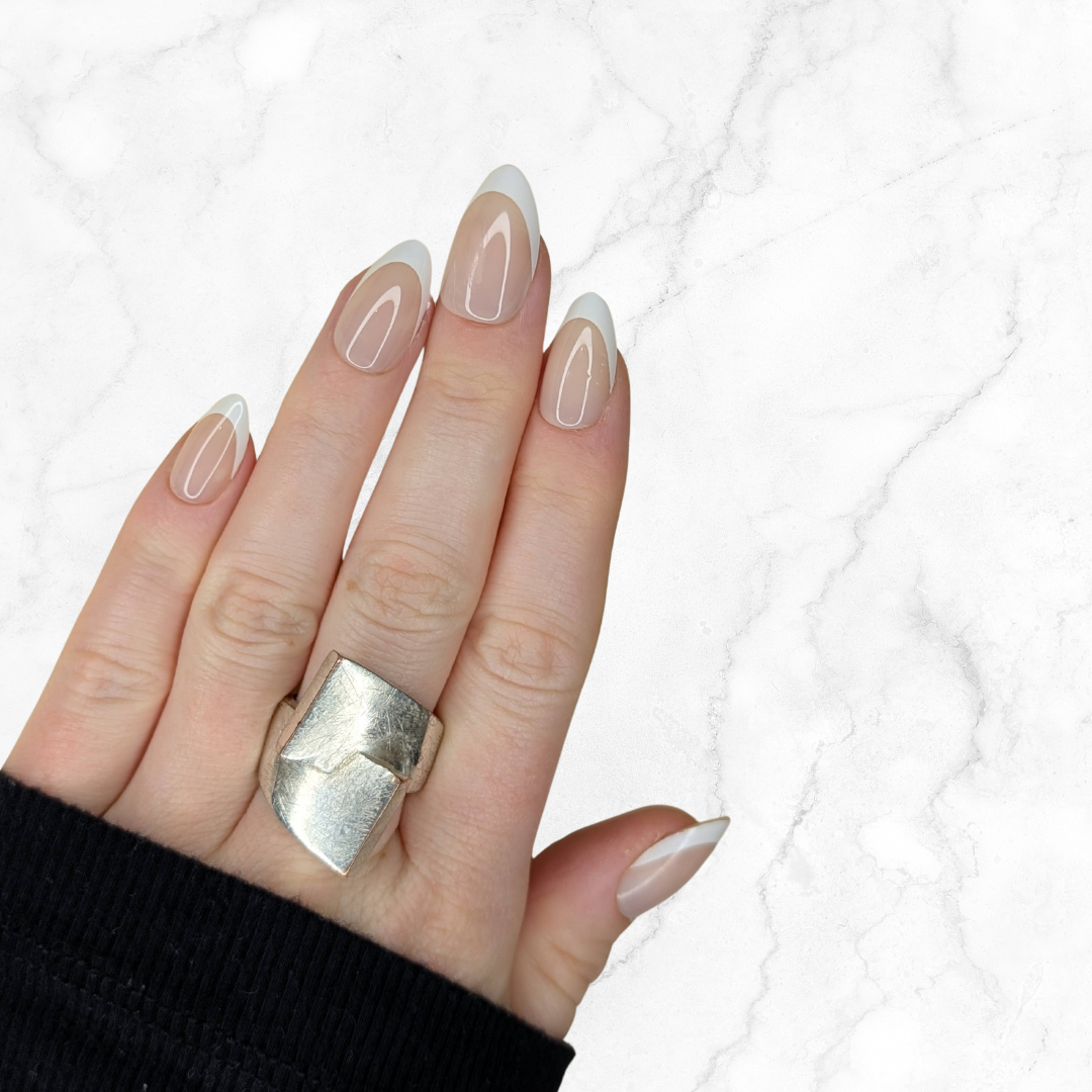 Left hand showing classic almond French tipped nails on a marble background.