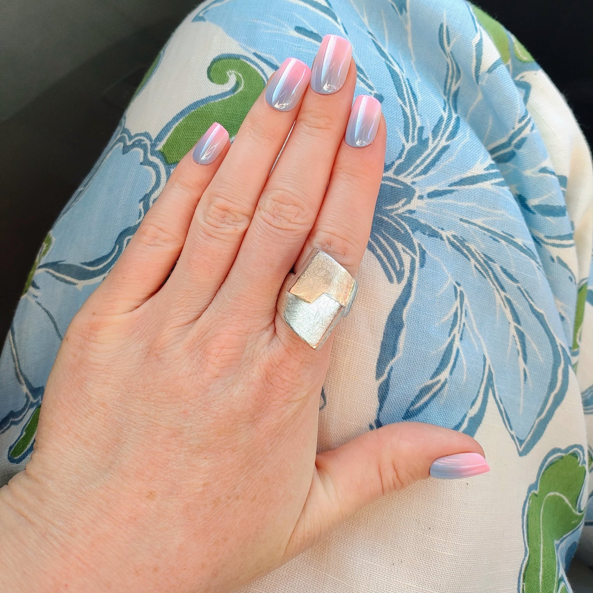Left hand showing square nails in a metallic ombre of blue and pink on a floral pant leg