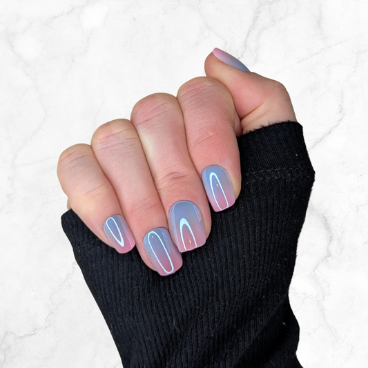 Right hand showing square nails in a metallic ombre of blue and pink against a marble background.