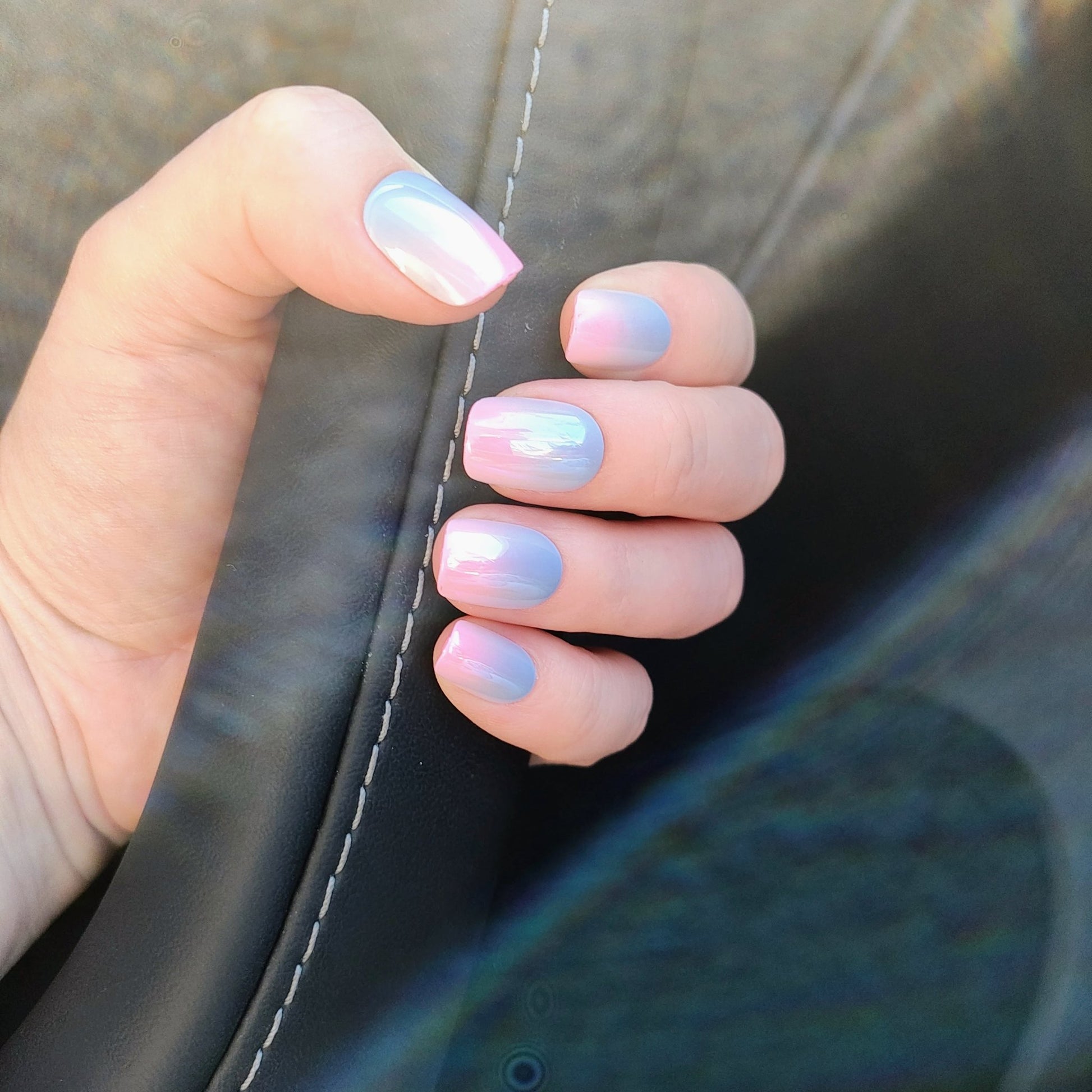 Left hand showing square nails in a metallic ombre of blue and pink holding a car door handle.
