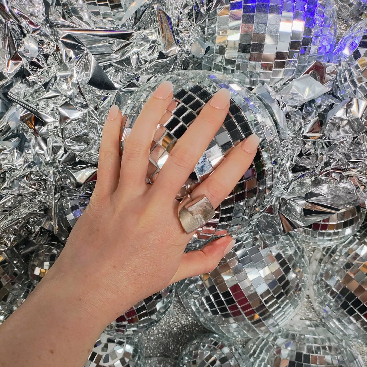 Left hand showing square nails with an ombre effect of peach to white holding a disco ball on a disco ball wall.