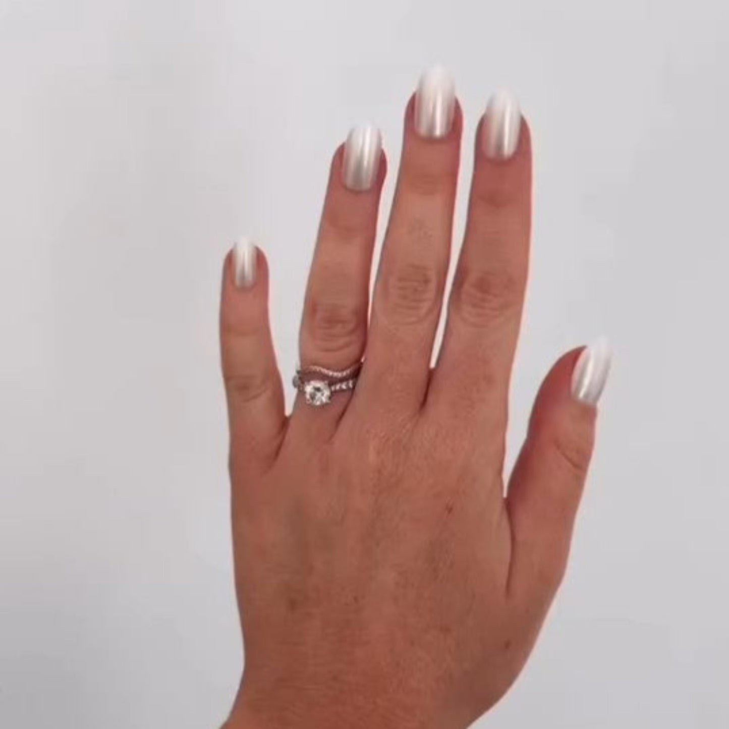 Left hand showing oval pearl coloured nails on a white wall.