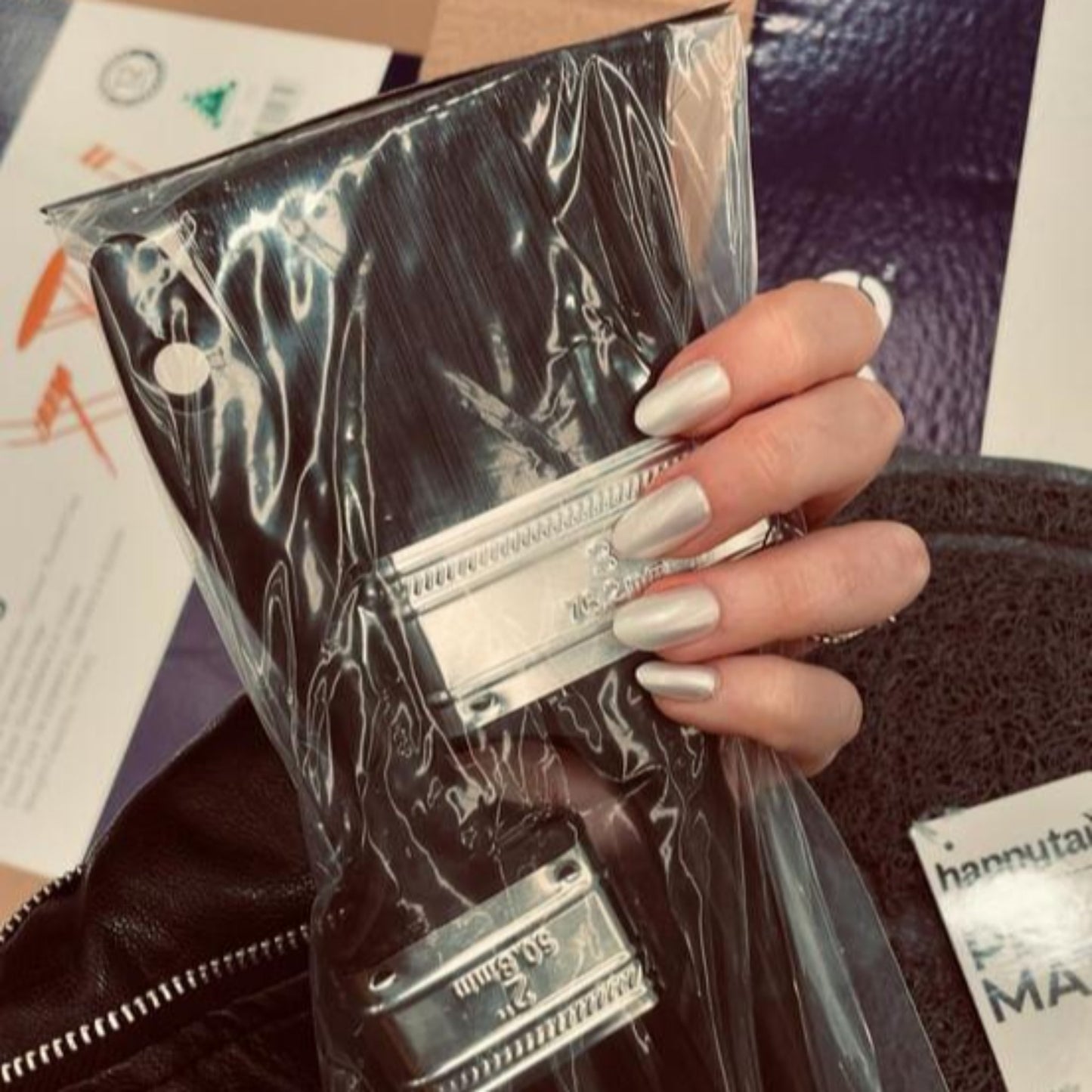 Left hand wearing oval pearl coloured nails holding a packet of paintbrushes.