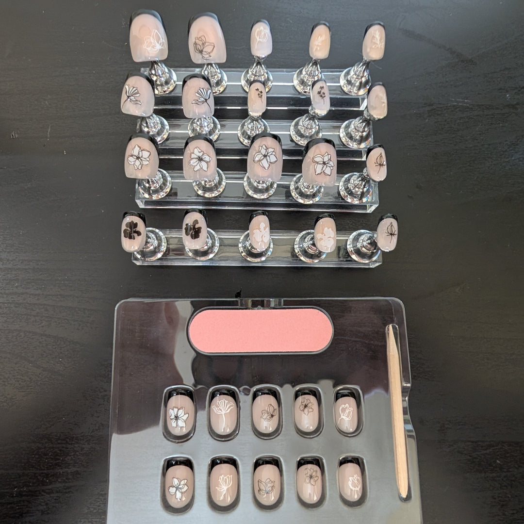 Image of 20 Snap Nails in Signature collection square black french tip nails with black and white fine black and white details on little nail pedestals. Below this is a box of 10 nails with a nail file and cuticle stick.