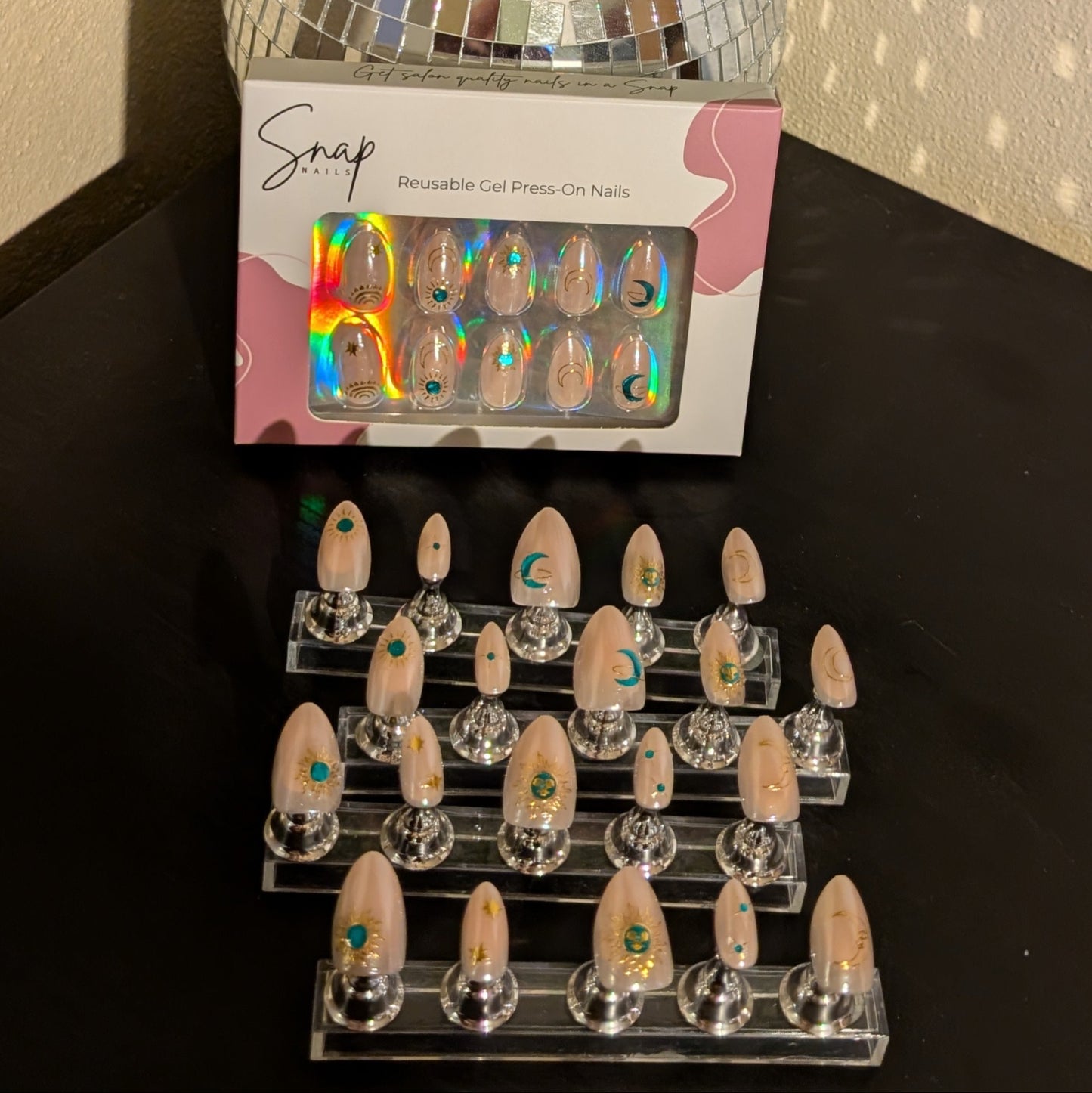 Image of 20 Snap Nails in Signature collection almond star dust nails with gold details on little nail pedestals. Above this is a box of 10 nails.