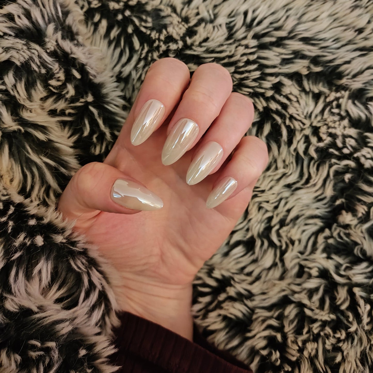 Left hand with long almond white pearl frosted nails on a faux fur blanket.
