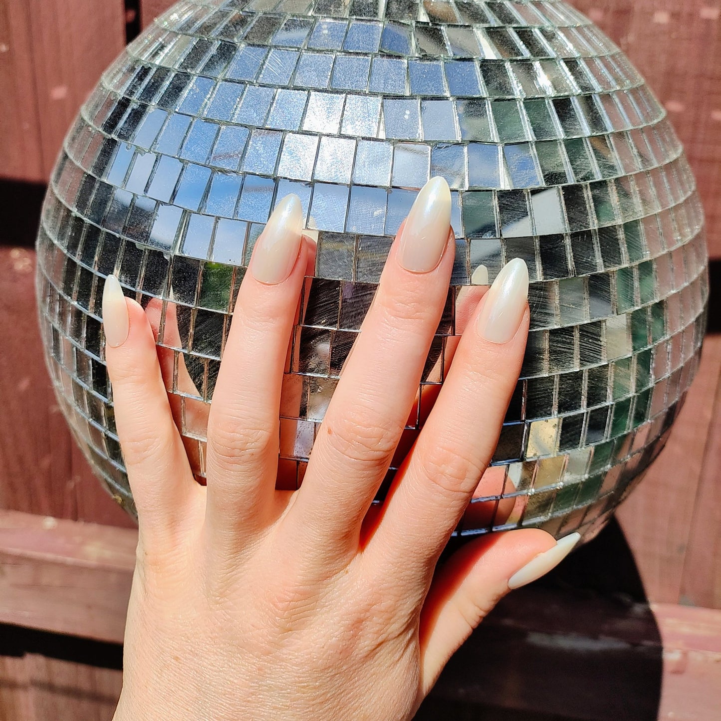 Left hand with long almond white pearl frosted nails in front of a disco ball.