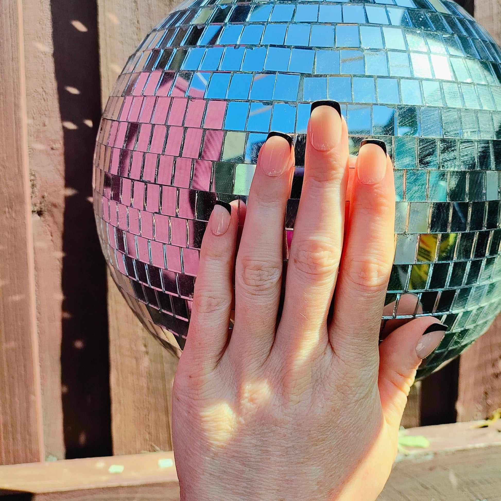 Left hand showing square nails with a black French tip on a disco ball background.