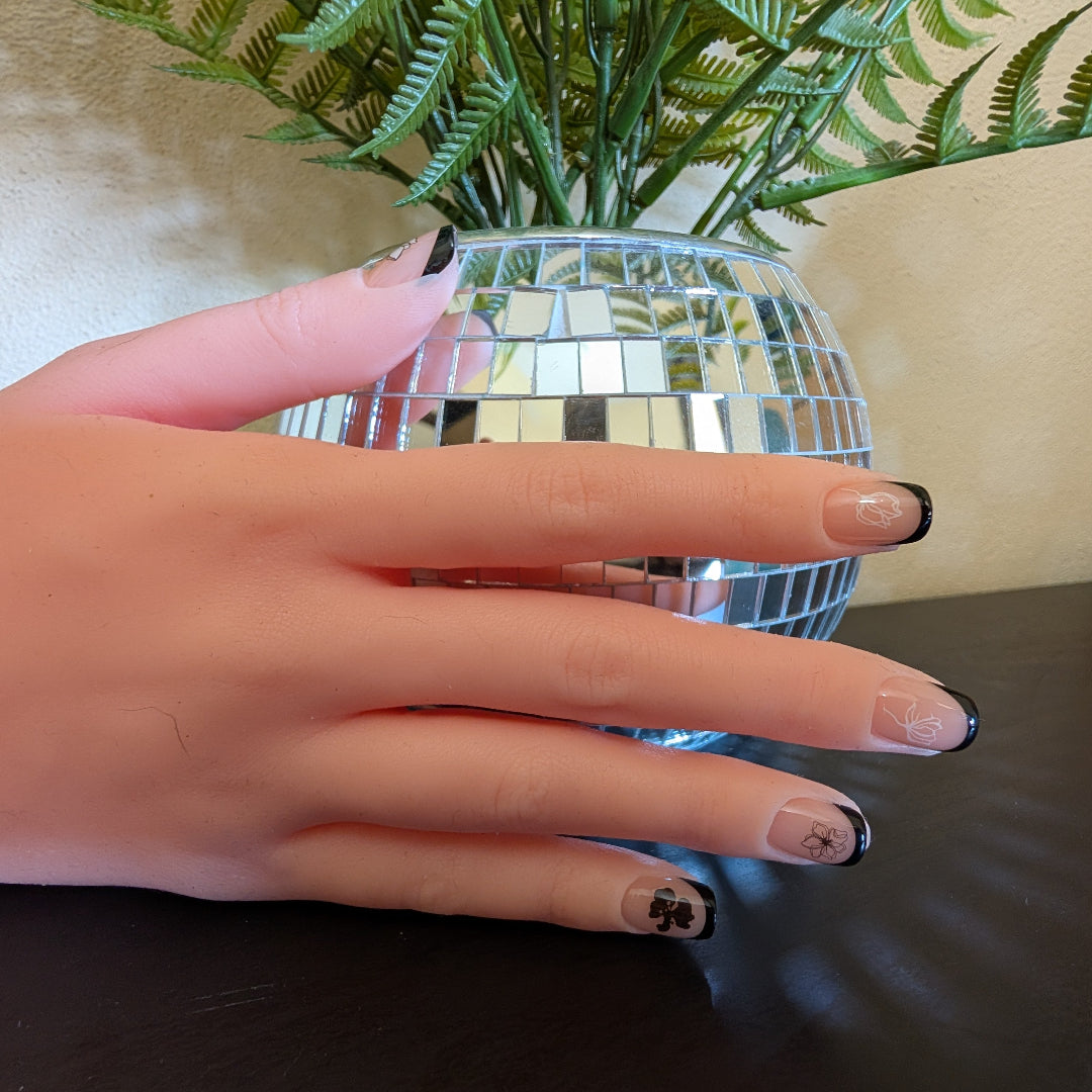 Image of a right hand wearing Snap Nails in Signature collection of 5 square black french tip nails with black and white fine black and white details.