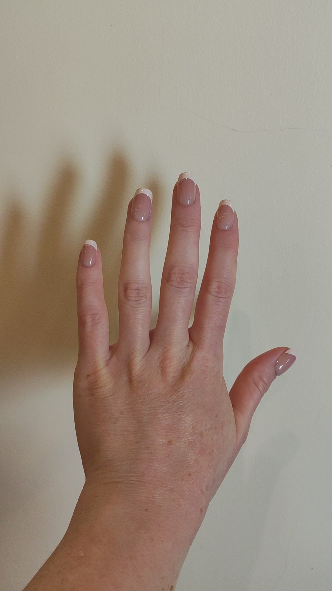Video of left hand showing classic square French tipped nails in front of a cream wall.