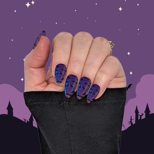 A left hand wearing medium long almond nails in a deep purple with small black bat details on a halloween background.