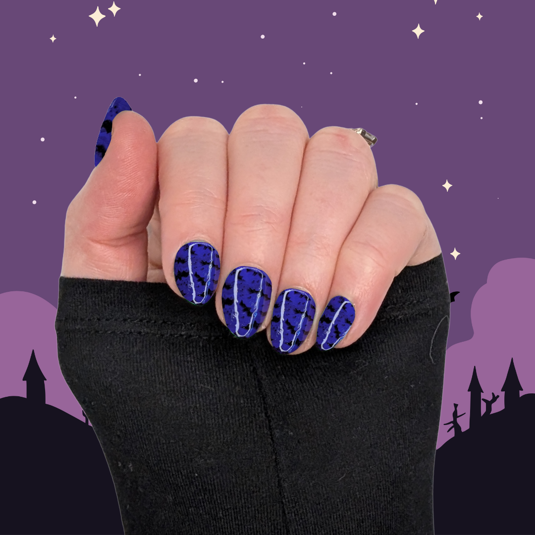 A left hand wearing XS almond nails in a deep purple with small black bat details on a halloween background.