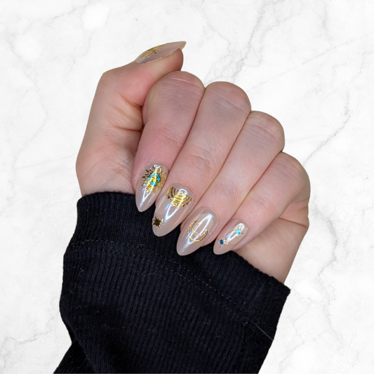 Image of a left hand wearing Snap Nails in Signature collection of 5 almond shimmery, peachy nails gold details on a marble background.