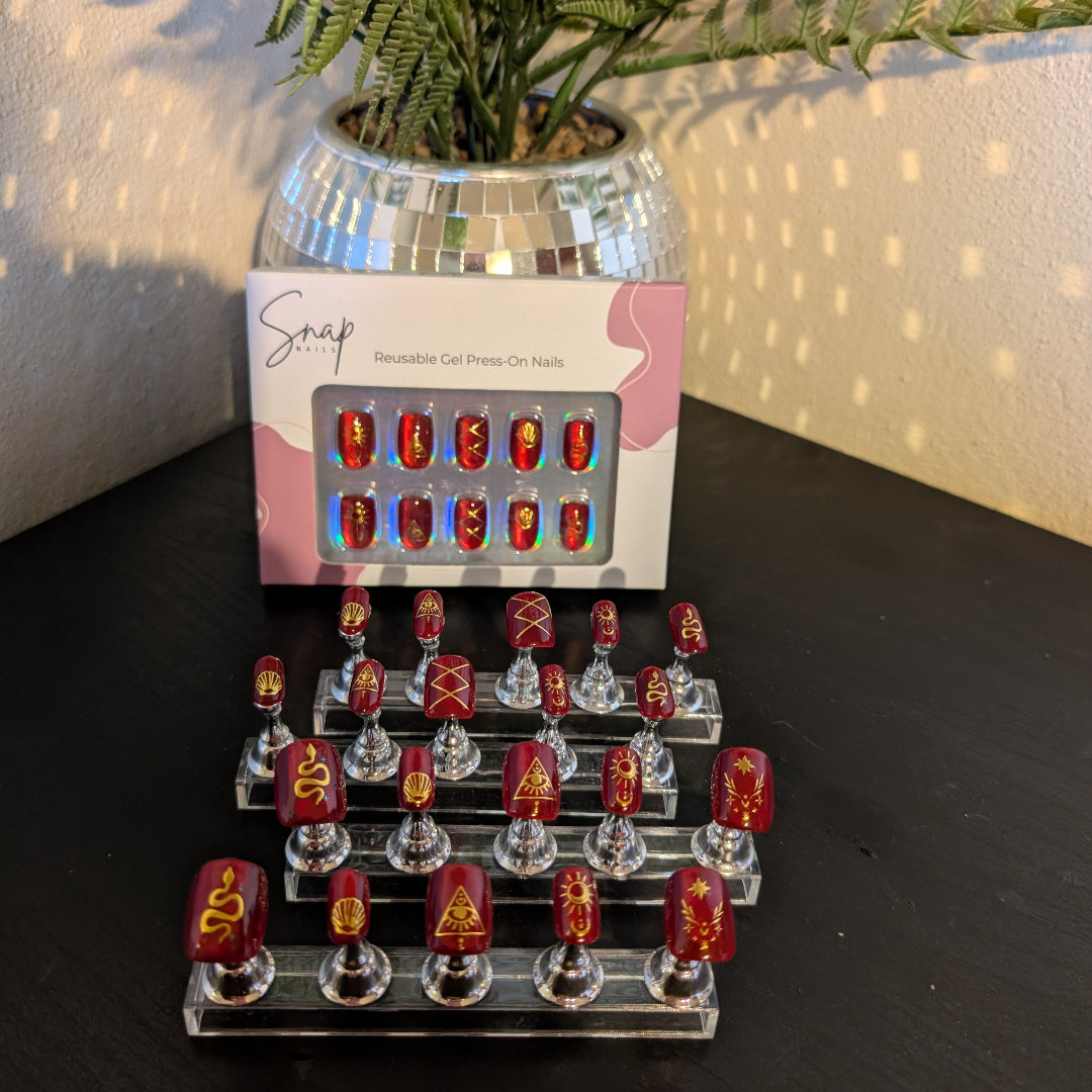 Image of 20 Snap Nails in Signature collection square cherry glaze nails with gold details on little nail pedestals. Above this is a box of 10 nails. 