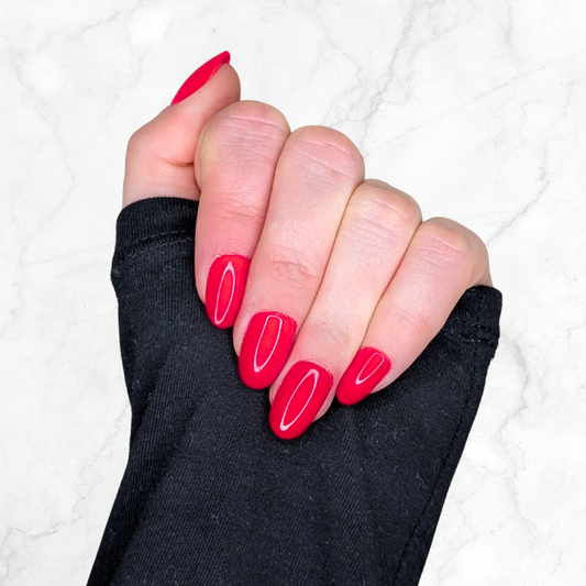 Left hand wearing oval cherry red nails on a marble background.