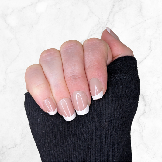Right hand showing five square french tipped nails on a marble background.