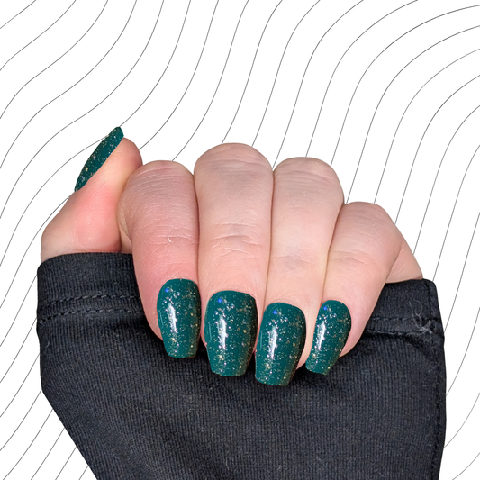 Left hand showing emerald green short coffin nails with a glitter gloss finish on a wavy background.