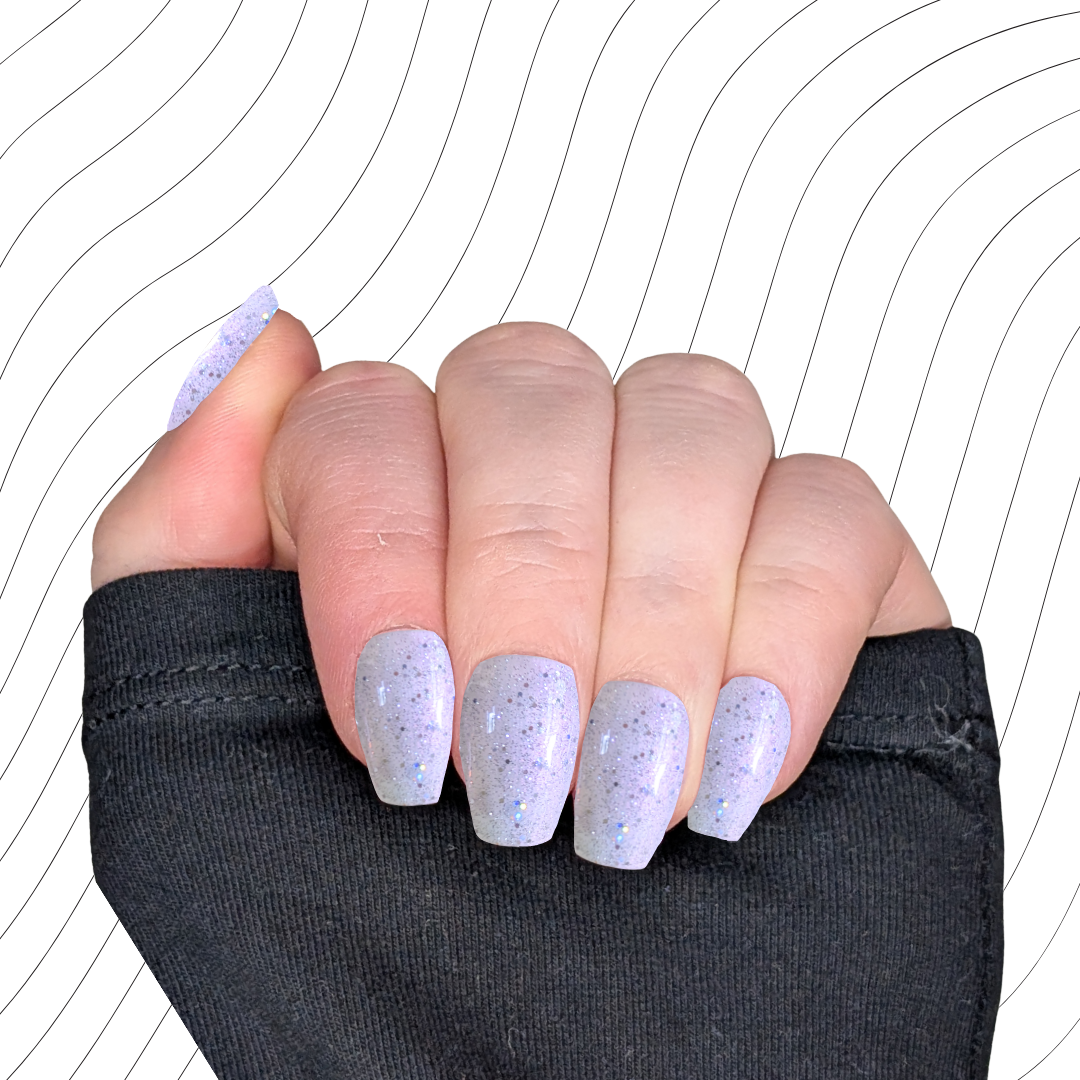 Left hand showing pearlescent white short coffin nails with a glitter gloss finish on a wavy background.