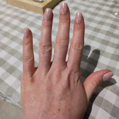 Left hand with square blush pink nails on a grey gingham table cloth.