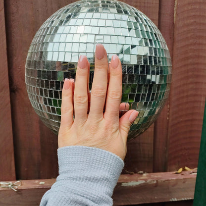 Left hand with square blush pink nails on a disco ball.