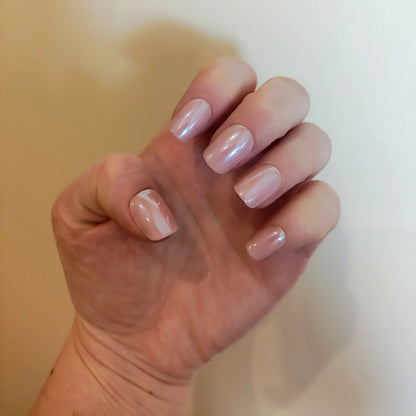 Left hand with square blush pink nails with a cream wall background.
