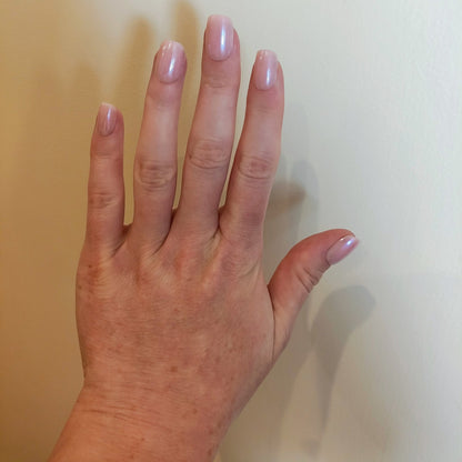 Left hand with square blush pink nails with a cream wall background.