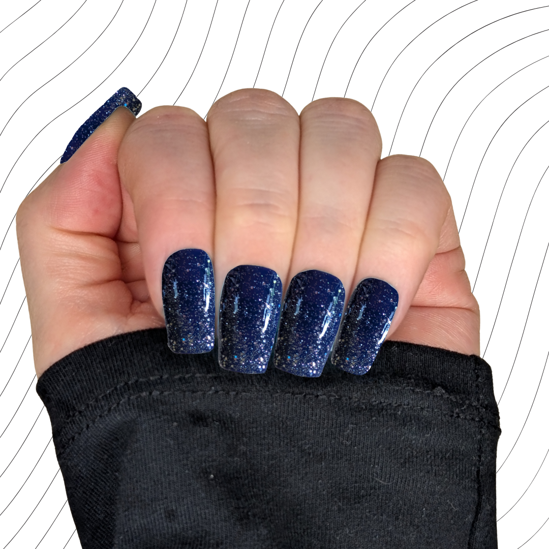 Left hand showing navy blue medium square nails with a glitter gloss finish on a wavy background.