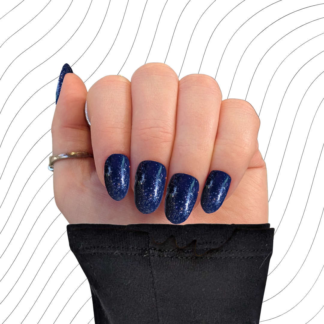 Left hand showing navy blue short oval nails with a glitter gloss finish on a wavy background.
