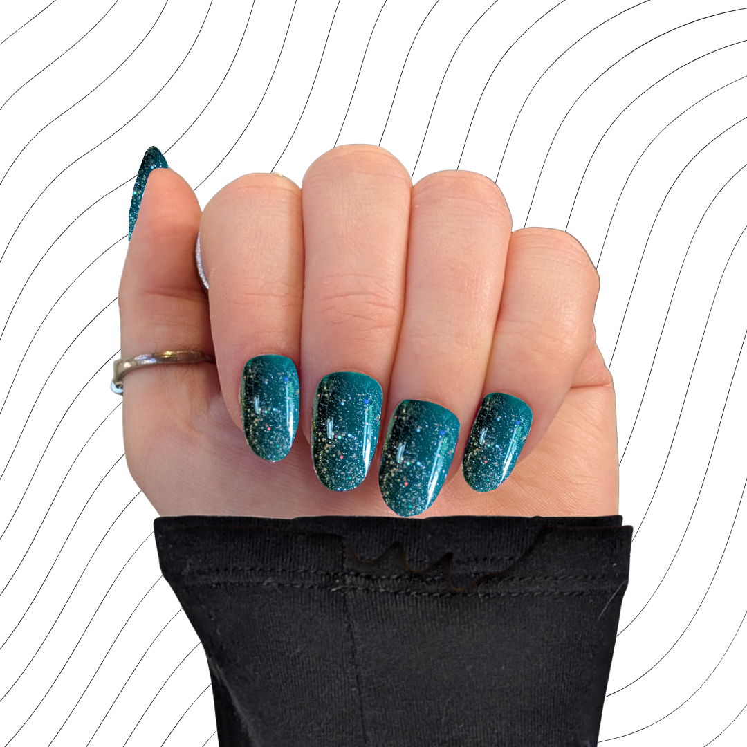 Left hand showing emerald green oval nails with a glitter gloss finish on a wavy background.