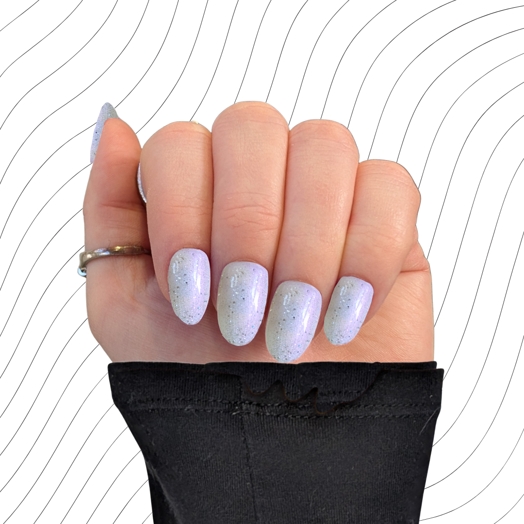 Left hand showing pearlescent white short coffin oval with a glitter gloss finish on a wavy background.