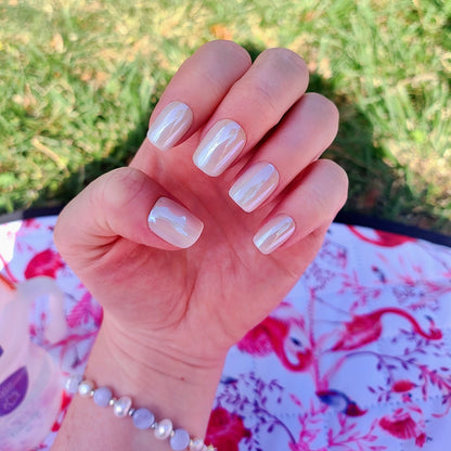 Left hand showing square pearl coloured nails on a pink and white picnic rug.