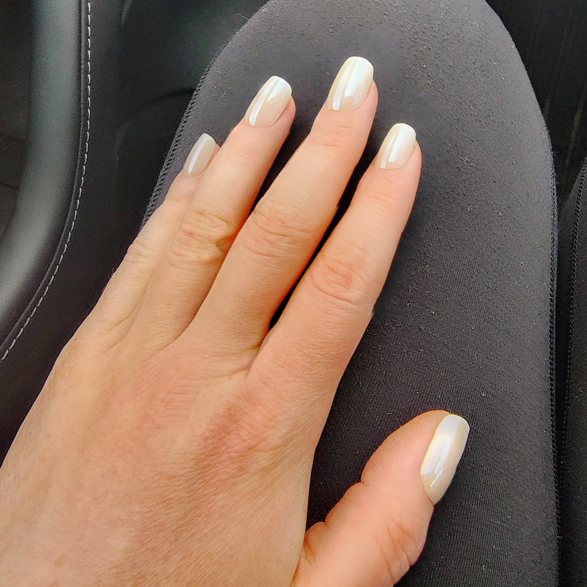 Left hand showing square pearl coloured nails on black leggings.