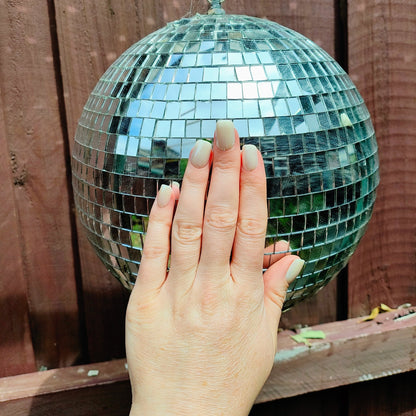 Left hand showing square pearl coloured nails on a disco ball.