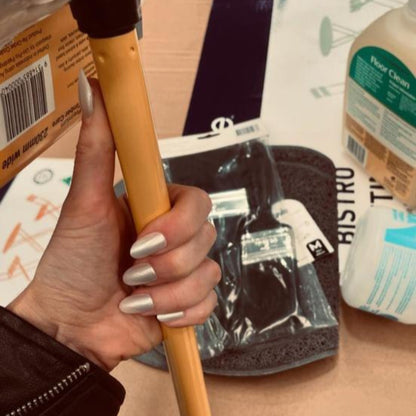 Left hand wearing oval pearl coloured nails holding a broom in a hardware store.