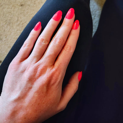 Left hand wearing oval red nails on a black leggings.